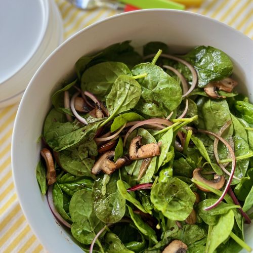 A white bowl filled with spinach, mushrooms and red onion.